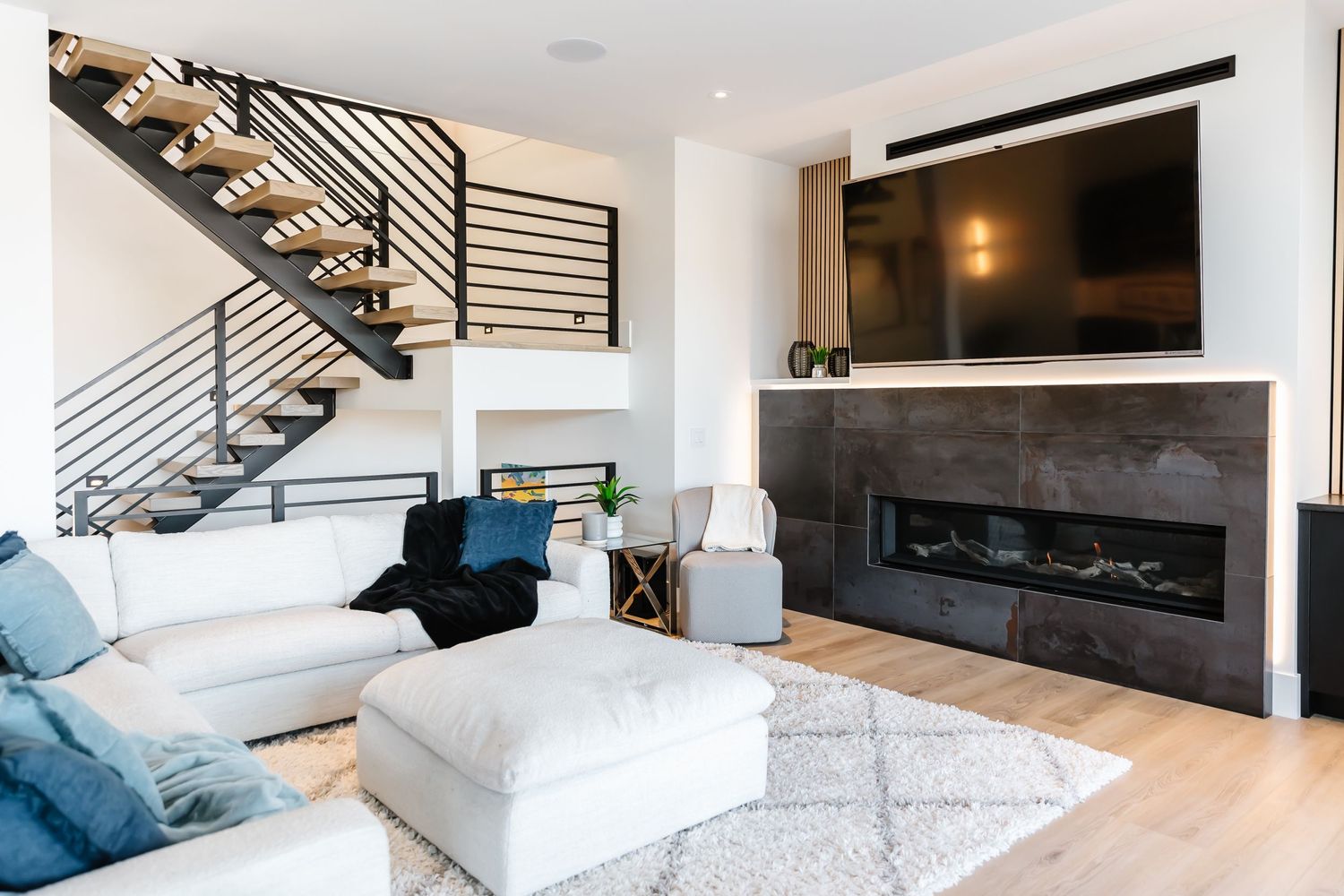 Contemporary living room with white sectional sofa, modern fireplace, and black metal staircase railing.