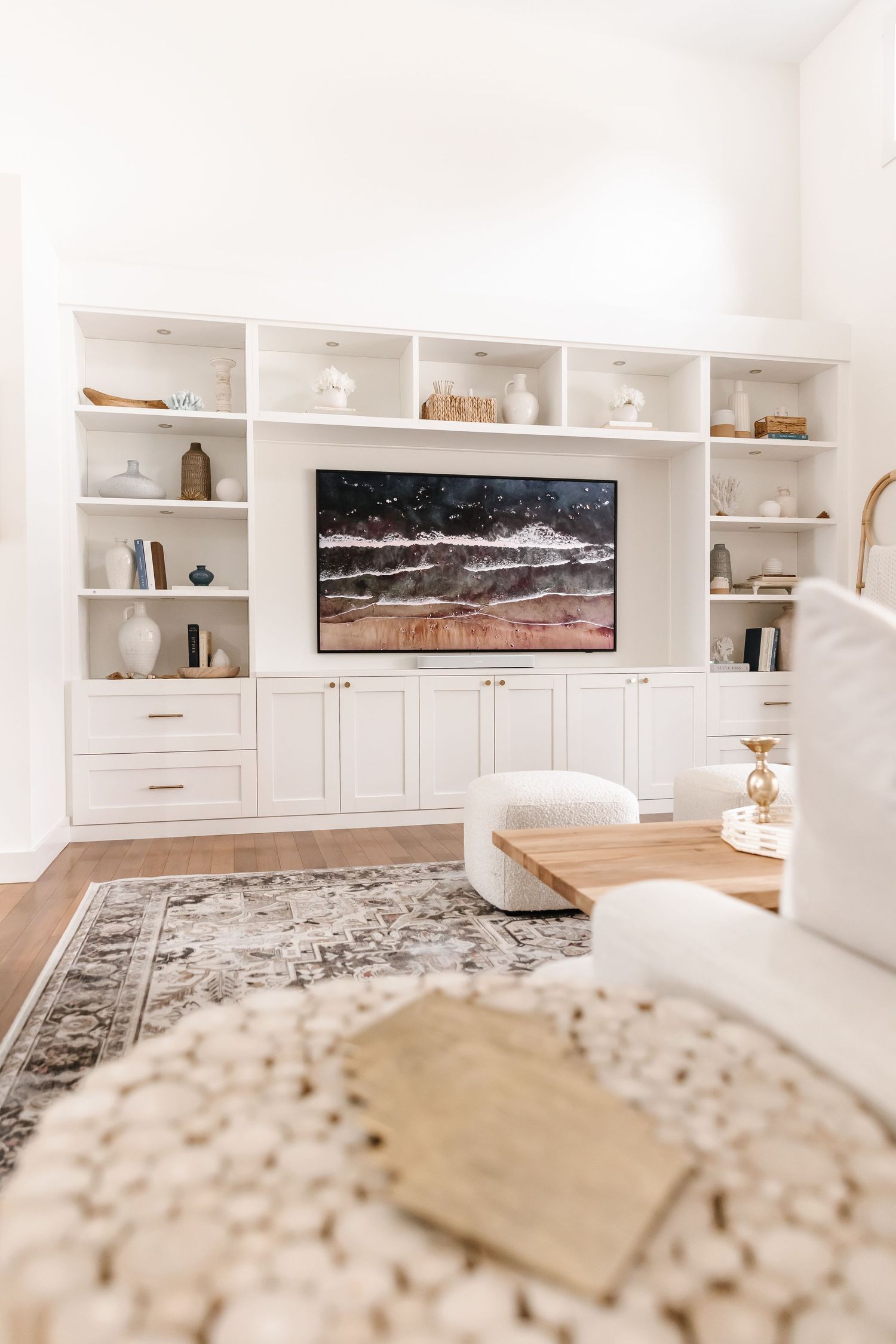 Custom white built-in entertainment center with wooden shelves and coastal artwork.