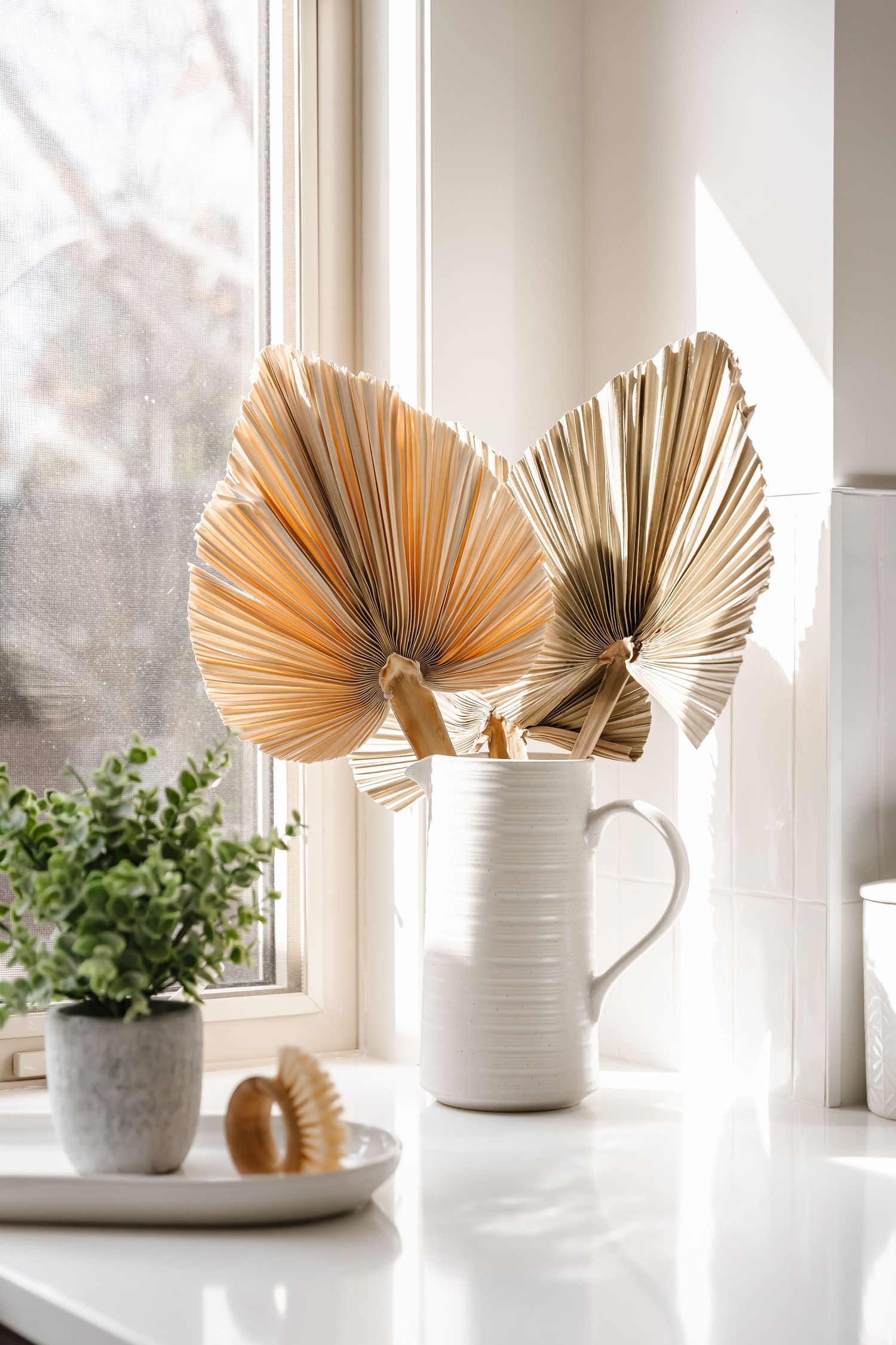 Decorative dried palm fans in white ceramic vases displayed on windowsill.