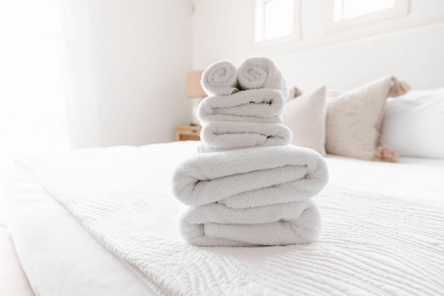 Neatly folded white towels stacked on white surface in bright room.