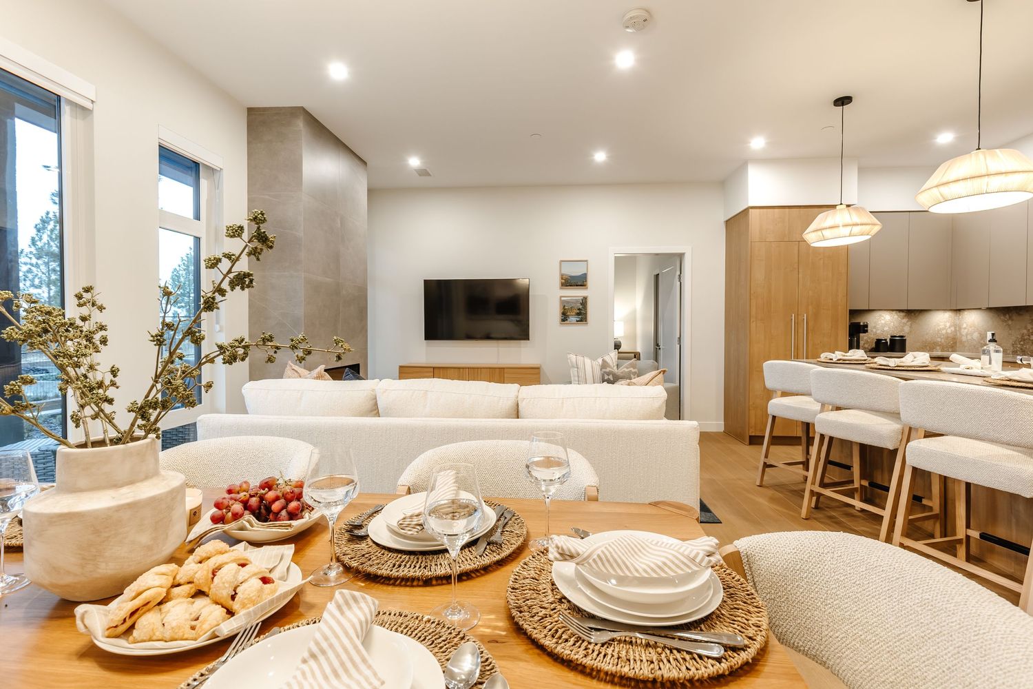 Modern open concept living space with white and wood accents showcasing dining area and kitchen with pendant lighting.