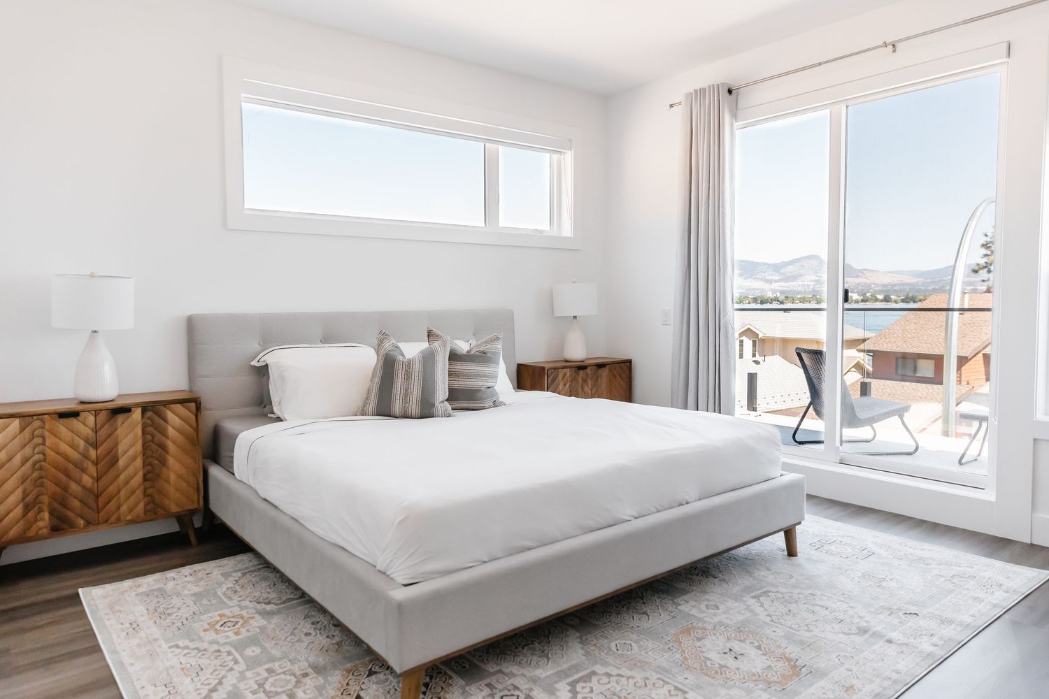 Bright modern bedroom with mountain views, grey upholstered bed, and chevron wood nightstands.