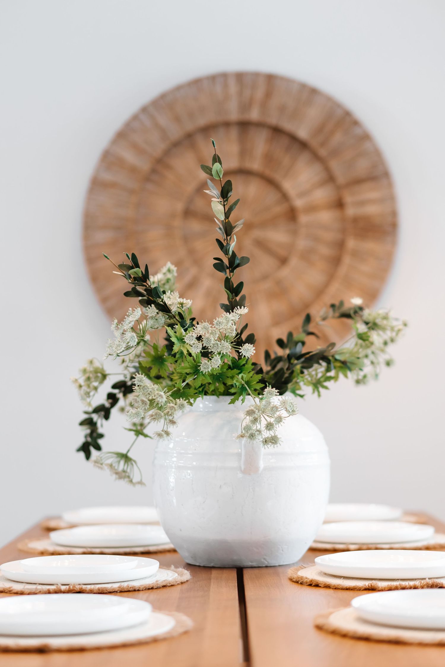 Elegant table setting with white plates and floral centerpiece on wooden charger.