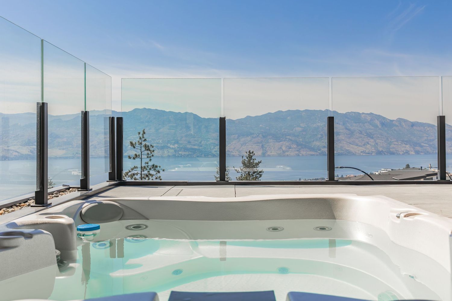 Rooftop hot tub with glass railings overlooking mountain landscape and blue skies at a west Kelowna Airbnb