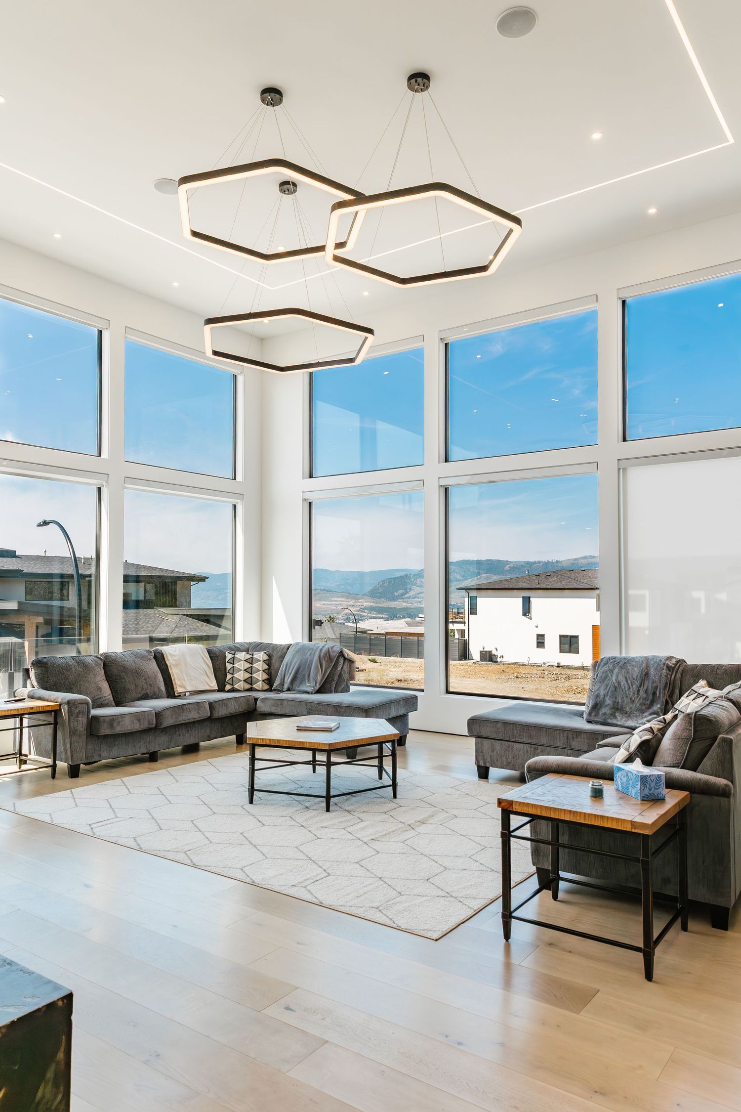 Modern living room with geometric ceiling lights, gray sofas, and stunning panoramic mountain views in a west Kelowna Airbnb