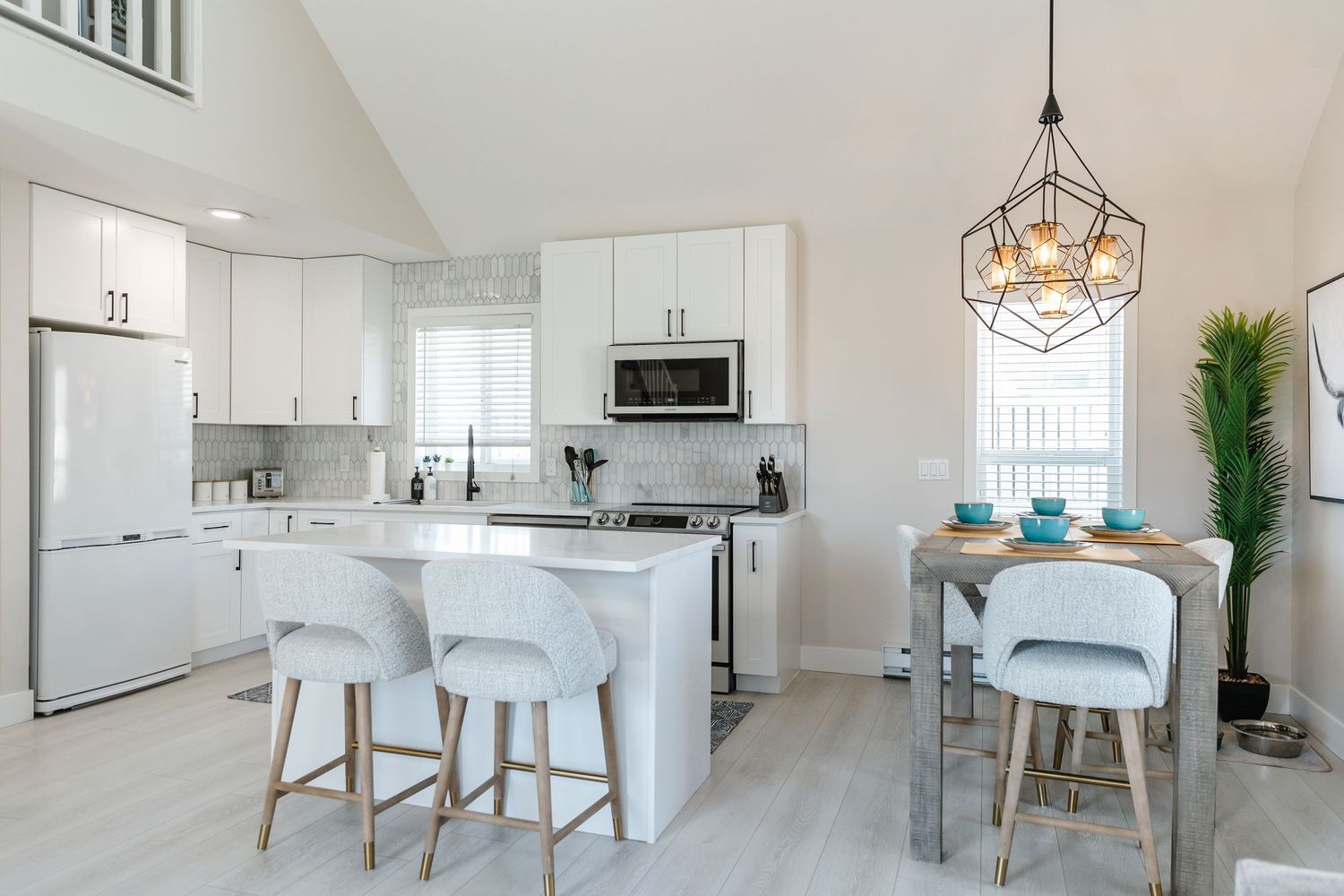 Contemporary white kitchen and dining area with geometric pendant lights and sleek bar seating.