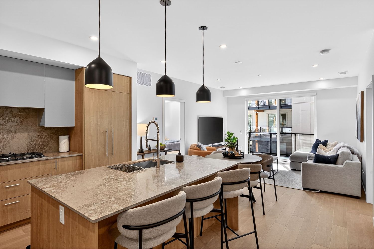 Modern open concept kitchen with granite countertops, wood cabinets, black pendant lights and bar seating overlooking living room.