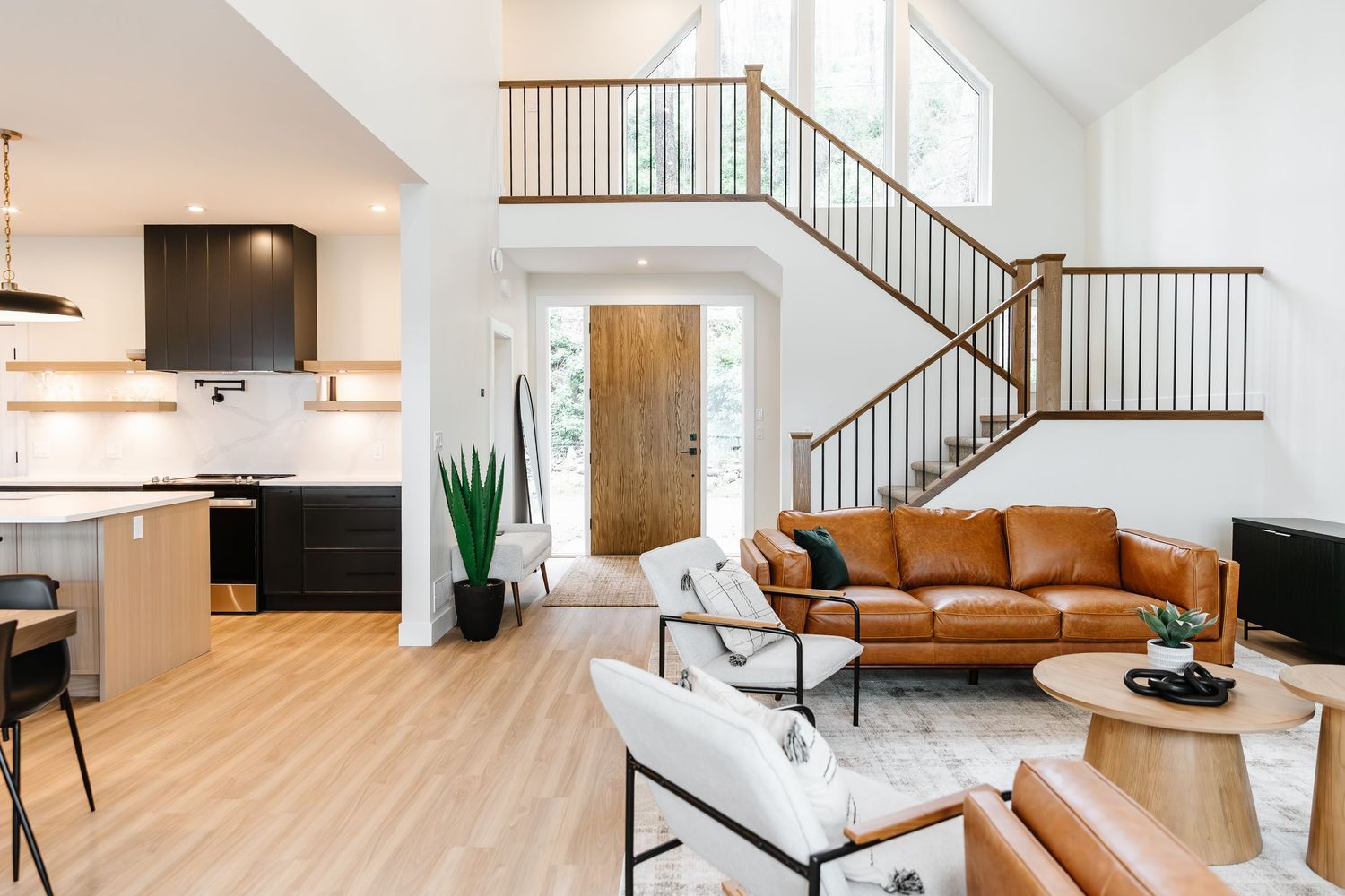 Modern living room with vaulted ceilings, leather sofa, and open staircase with wood railings in West Kelowna British Columbia Airbnb