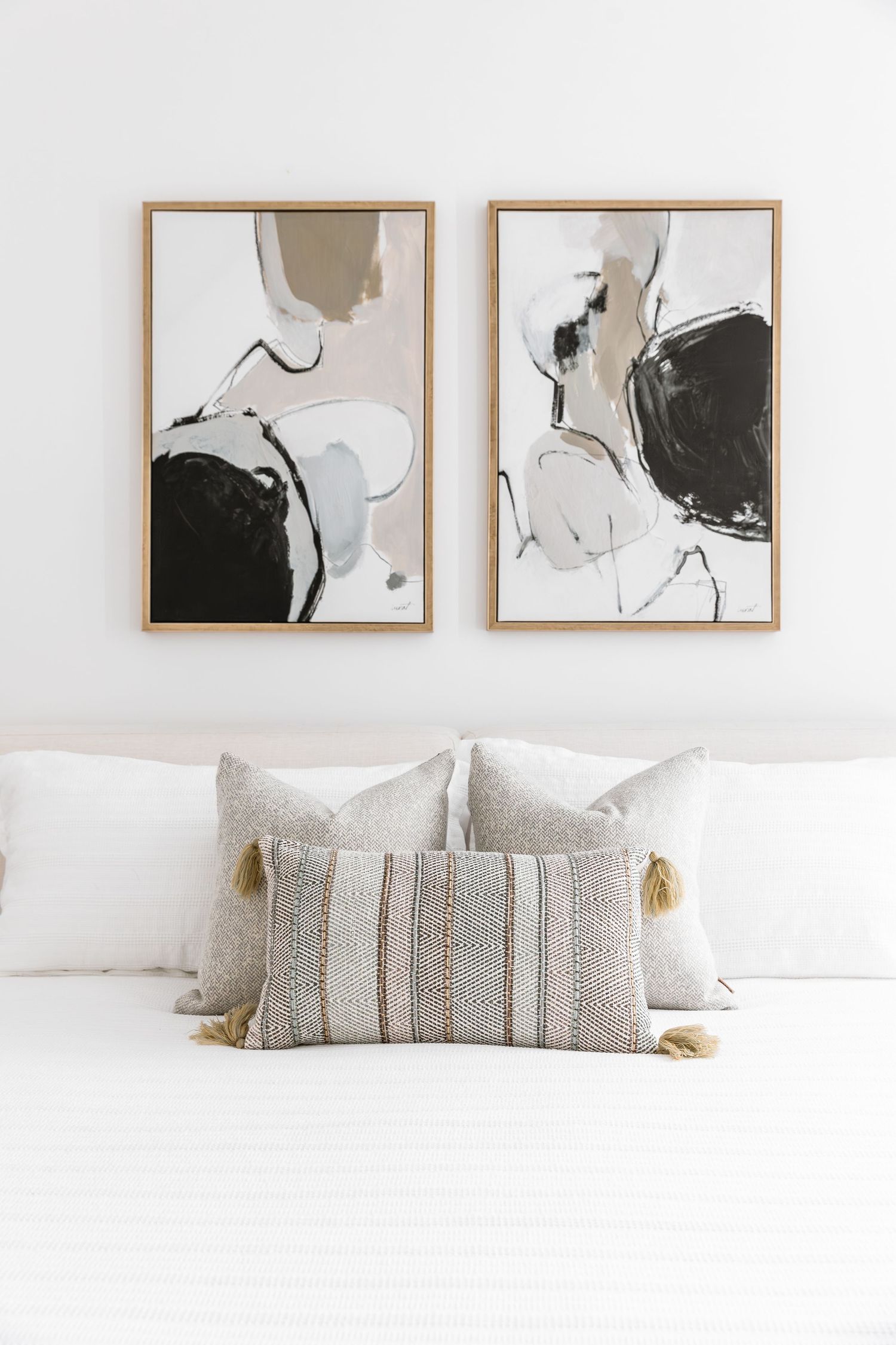 Abstract black and white art prints hanging above white bedding with textured throw pillows.