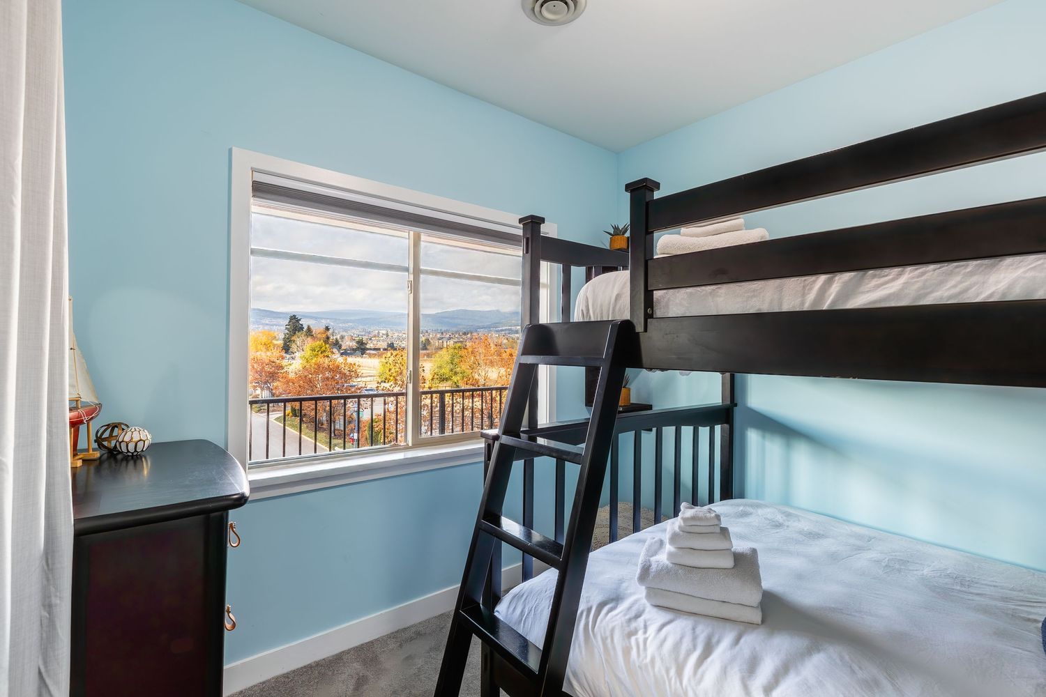 Modern bunk bed with ladder in a light blue room with white trim and hardwood flooring.