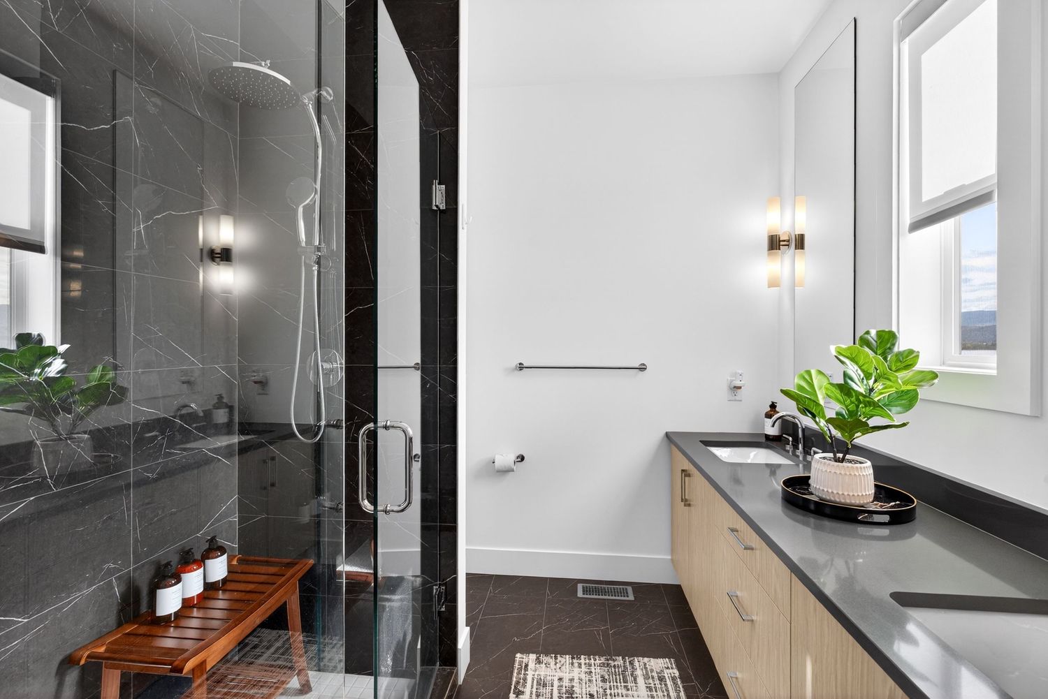 Modern bathroom with dark marble shower, wood vanity, black countertop, and elegant wall sconces.