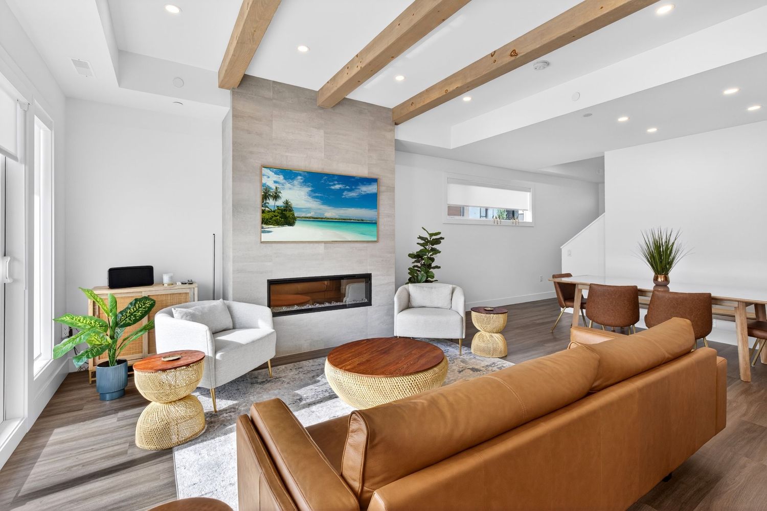 Modern living room with leather sofa, wood beam ceiling, stone fireplace, and bright coastal decor.
