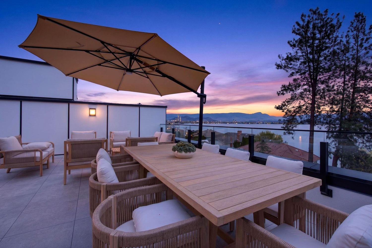 Rooftop patio with wooden dining table, cantilever umbrella, and stunning lake sunset views at dusk.
