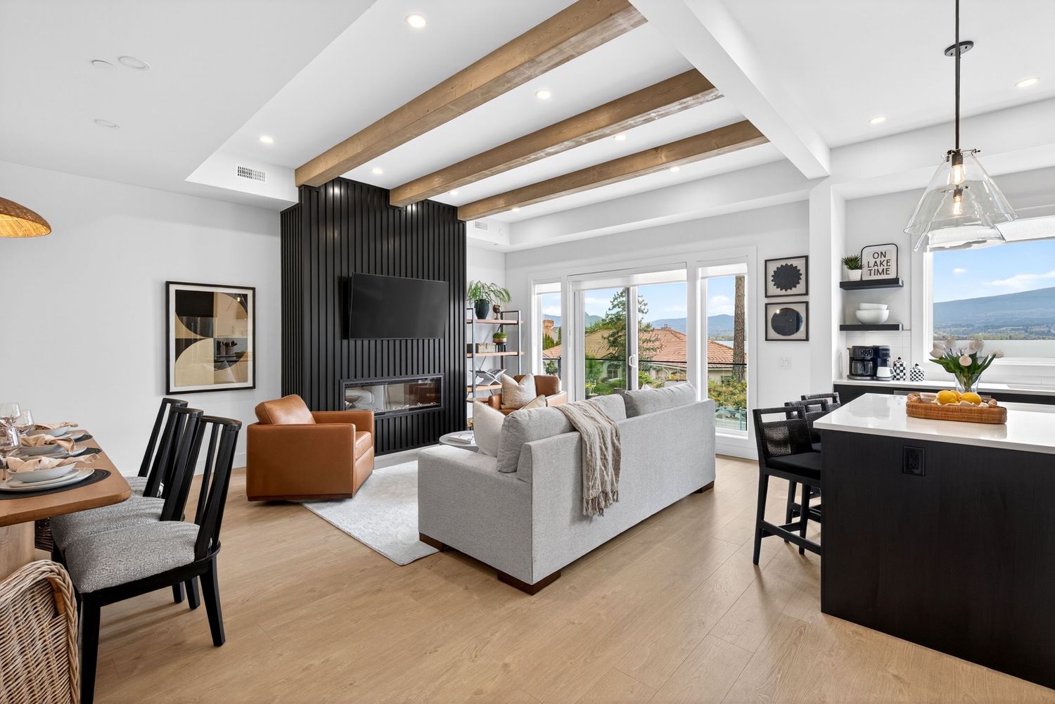 Modern open-plan living room with wood beam ceiling, white sofa, black fireplace wall, and mountain views.
