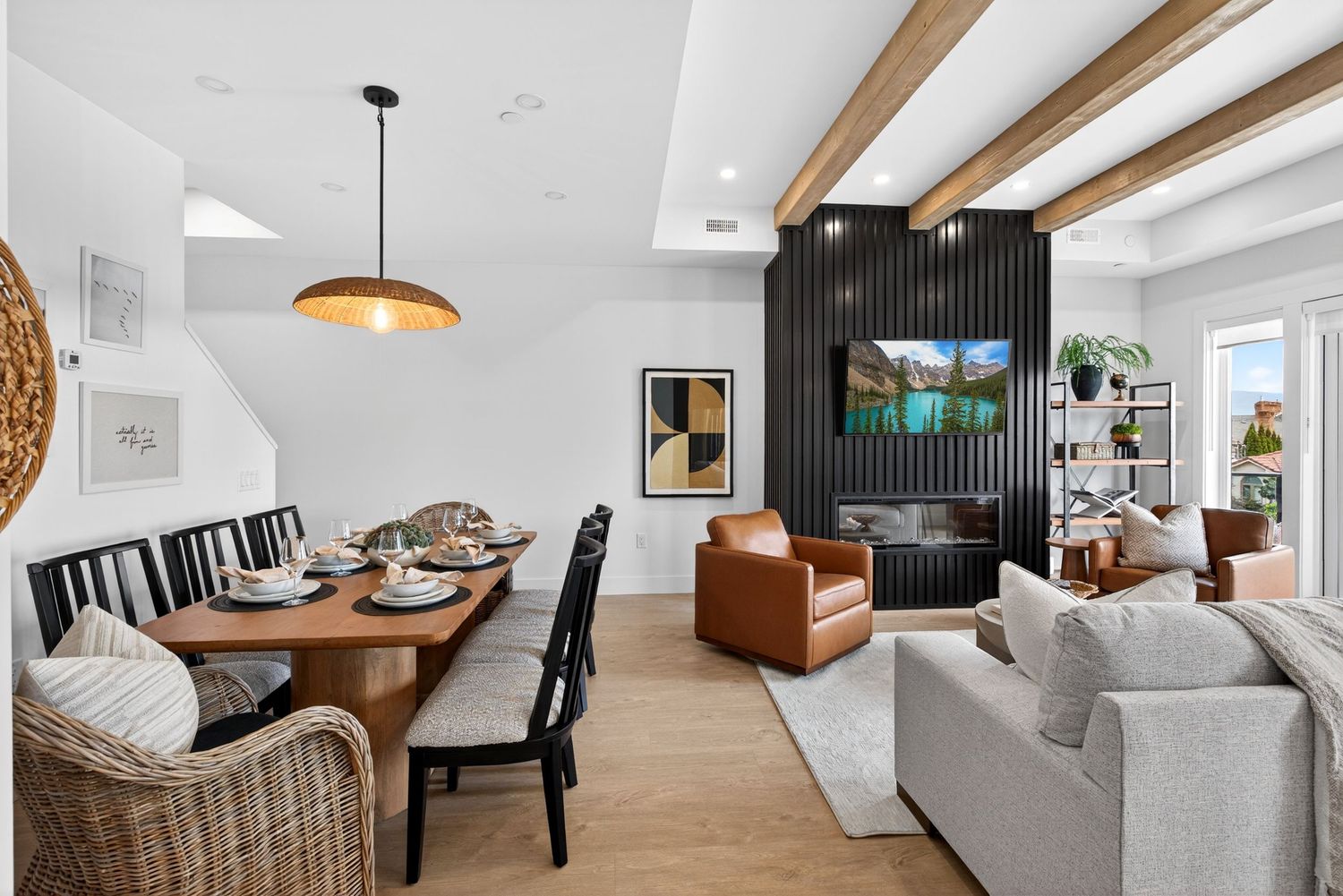 Modern open-plan living and dining room with wood beam ceiling, black accent wall, leather chair, and pendant light.