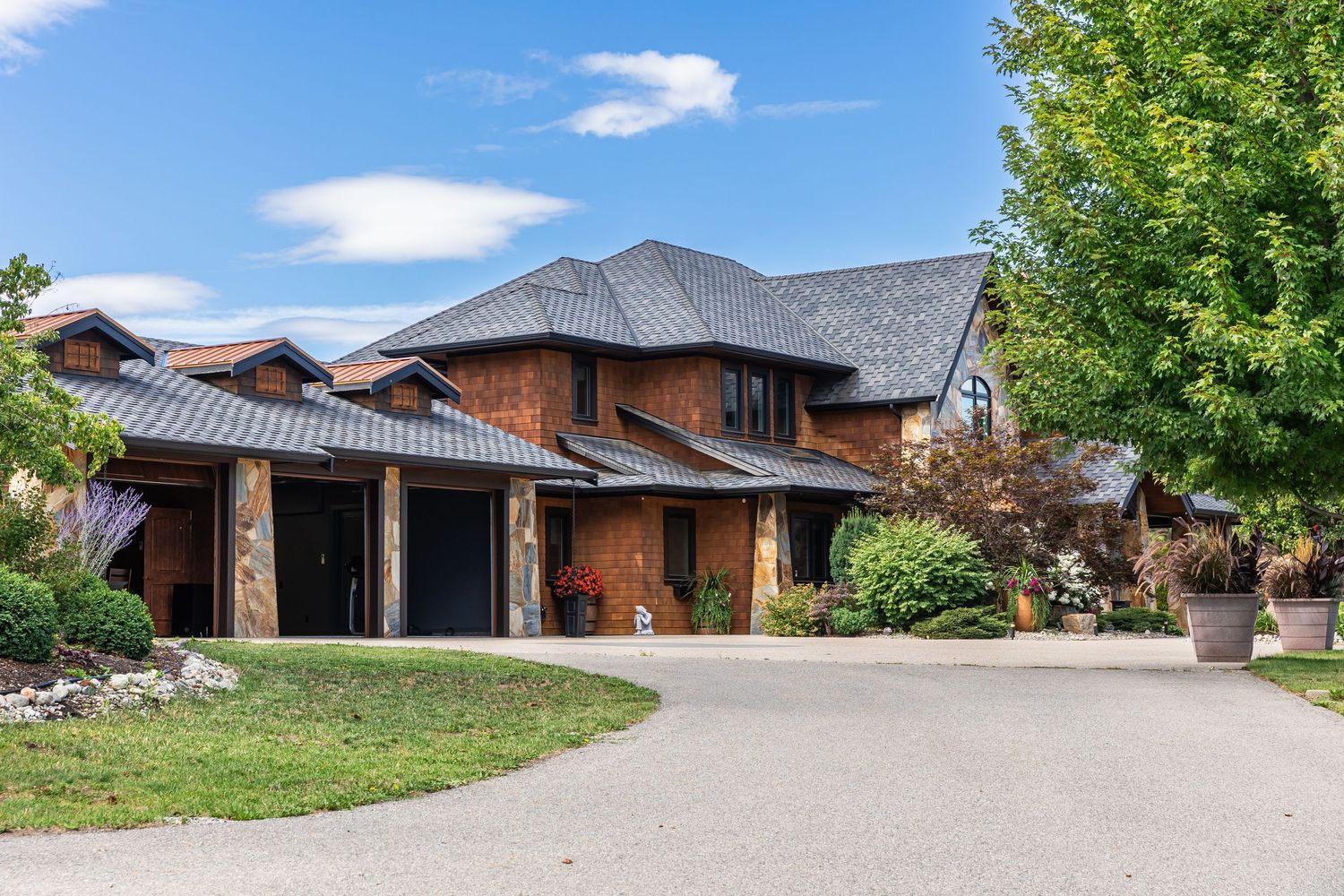 A panoramic view of a modern brick Airbnb home with green landscaping and a curved driveway under blue skies in Kelowna BC