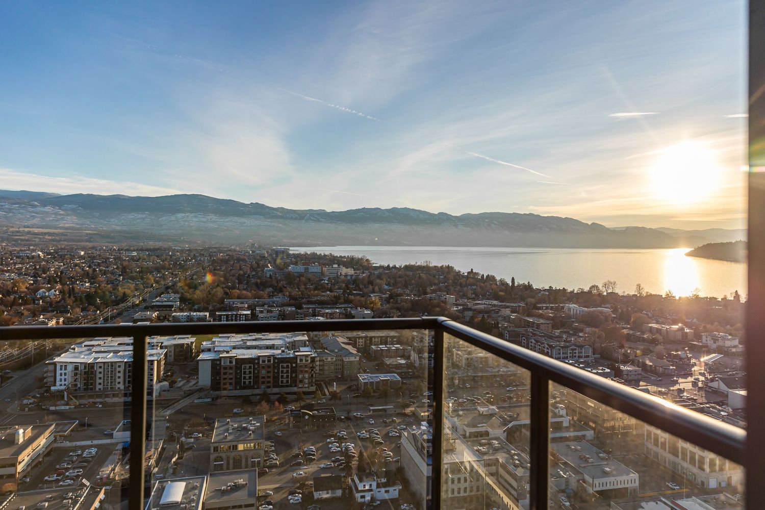 Panoramic cityscape view at sunset with mountains and water in the background.