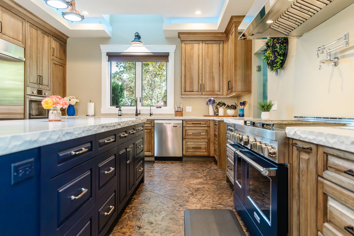Contemporary kitchen featuring navy blue lower cabinets and light wood upper cabinets with marble countertops.