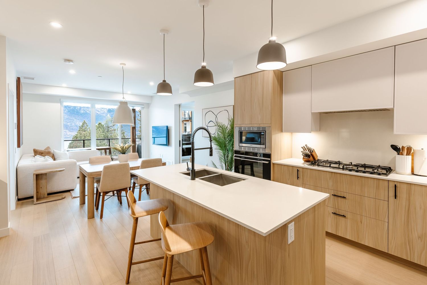 Modern minimalist kitchen with light wood cabinets, white countertops, and pendant lighting in an open concept layout.