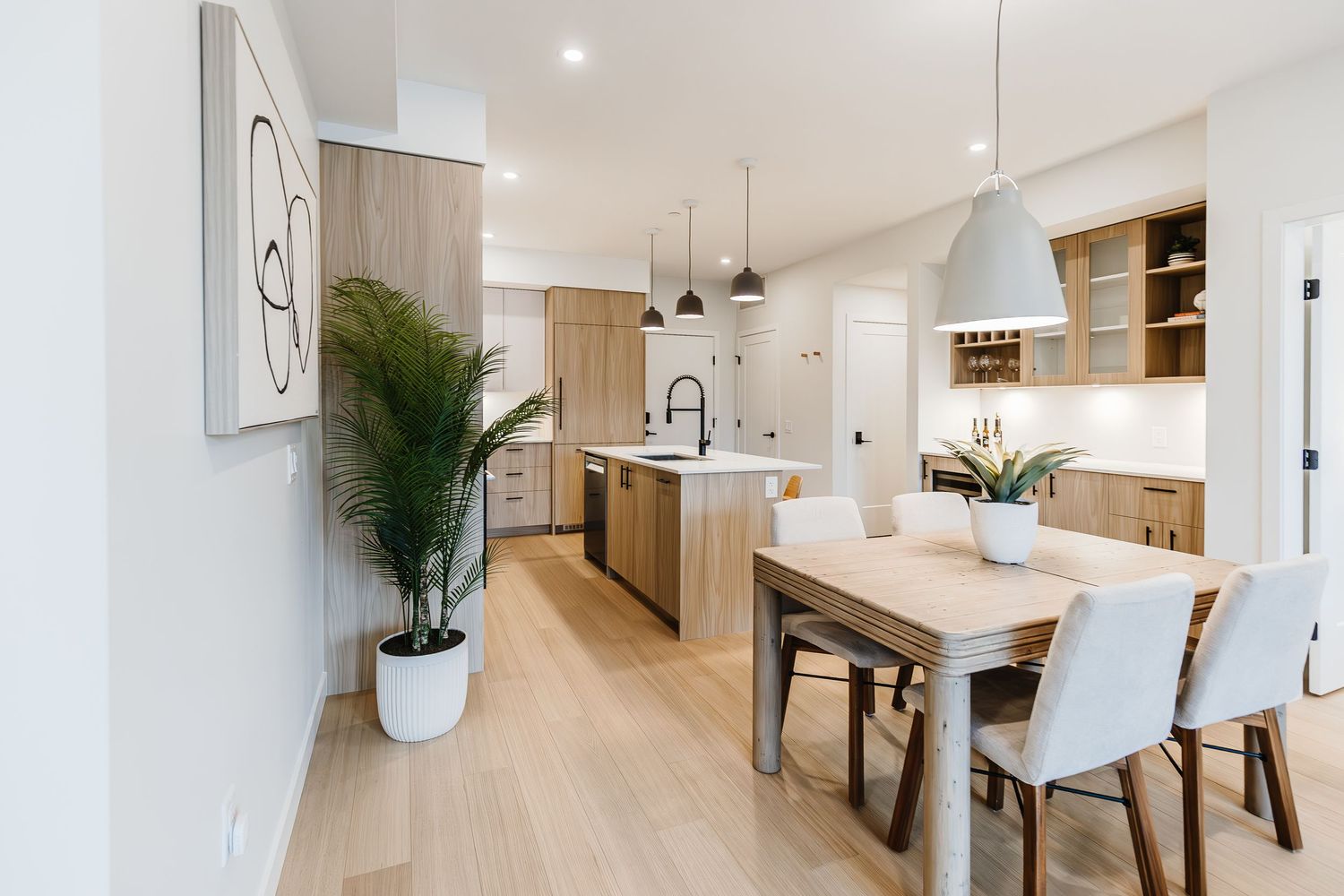 Modern open concept living space with white walls, hardwood floors, and minimalist dining area illuminated by recessed lighting.