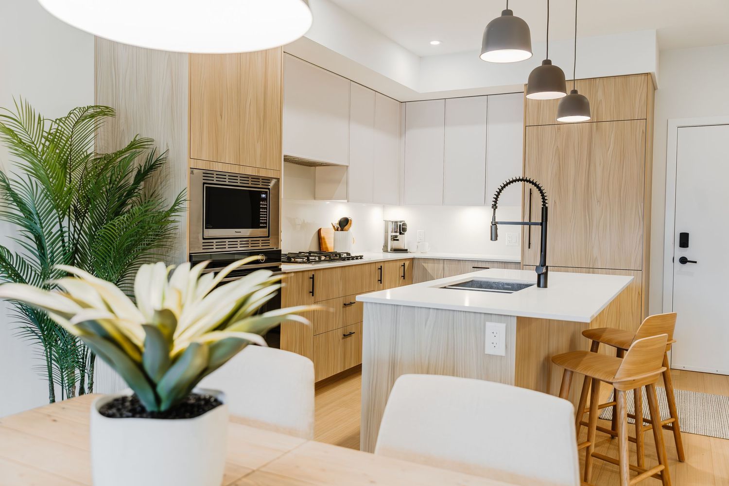 Modern minimalist kitchen and dining area with light wood accents, white cabinetry, and pendant lighting.