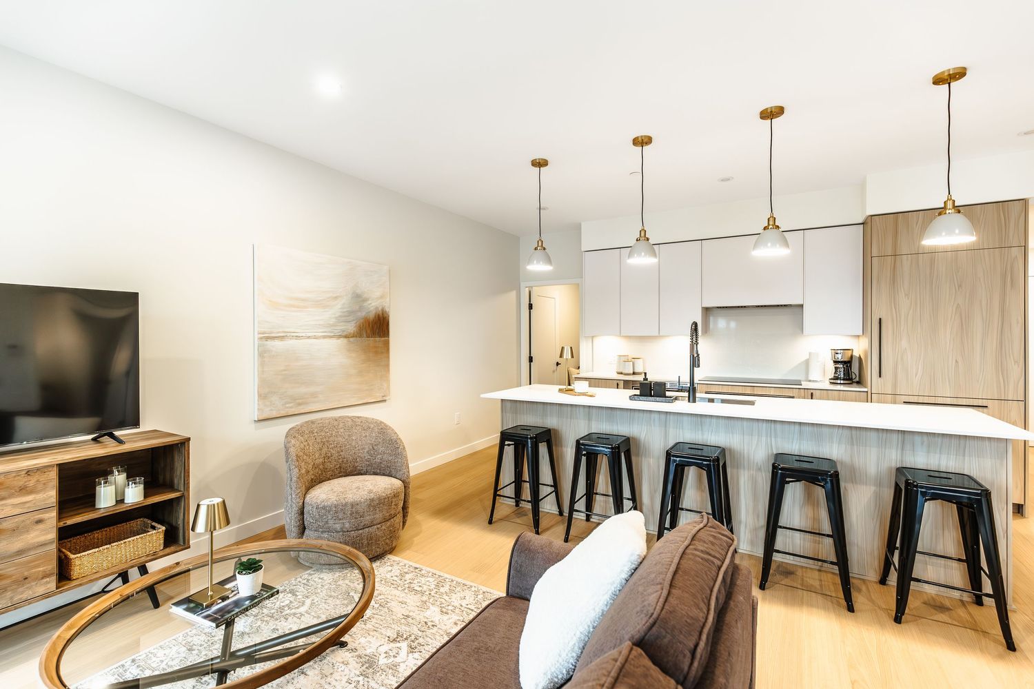 Modern open concept kitchen and living area with pendant lights, bar stools, and light wood accents.