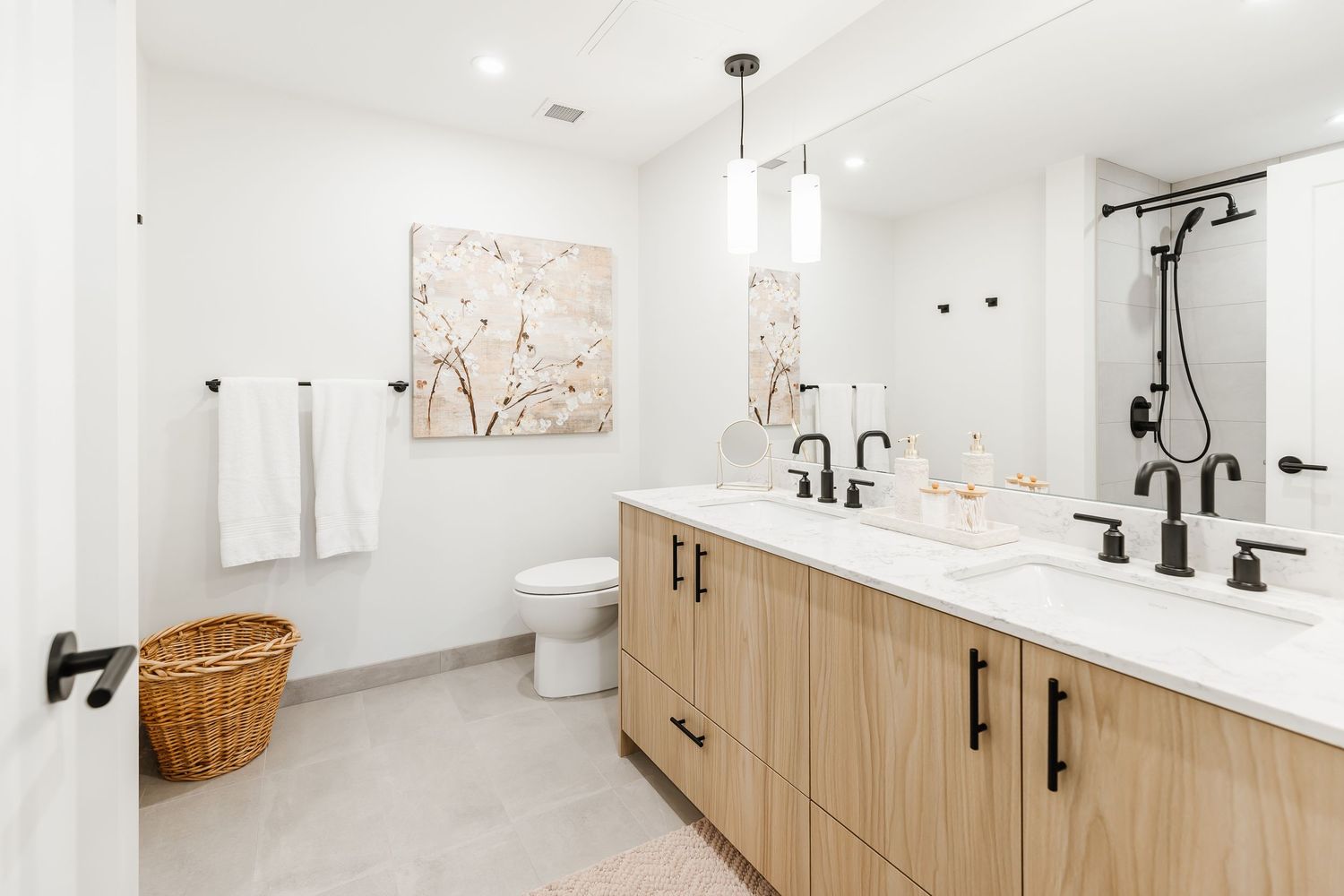 Modern bathroom interior with light wood vanity, white walls, and black fixtures showcasing minimalist design elements.