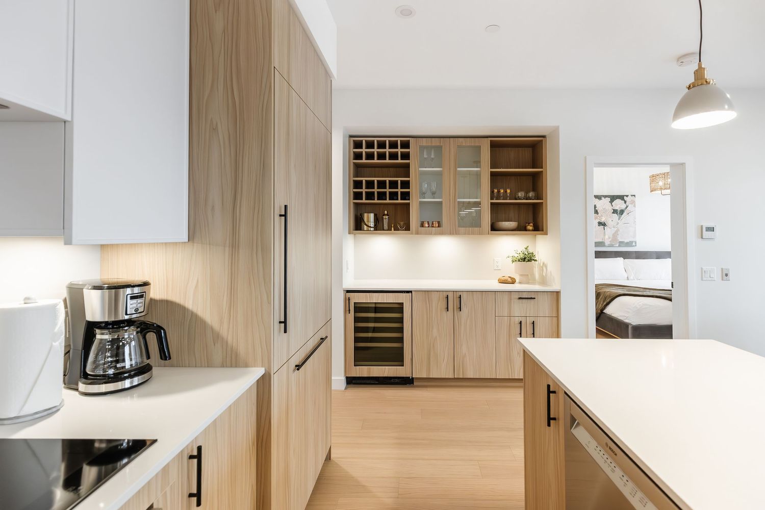 Modern kitchen interior with built-in wine storage, light wood cabinets, white countertops and hardwood flooring.