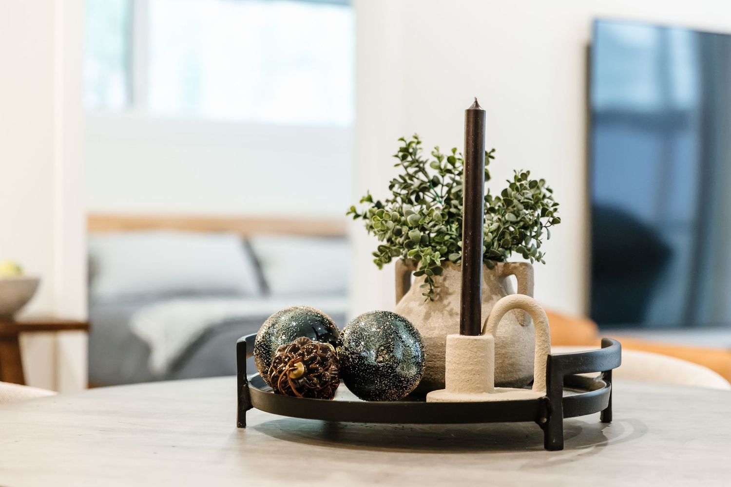 Modern minimalist living room decor with white candles and potted plants arranged on a black circular tray.