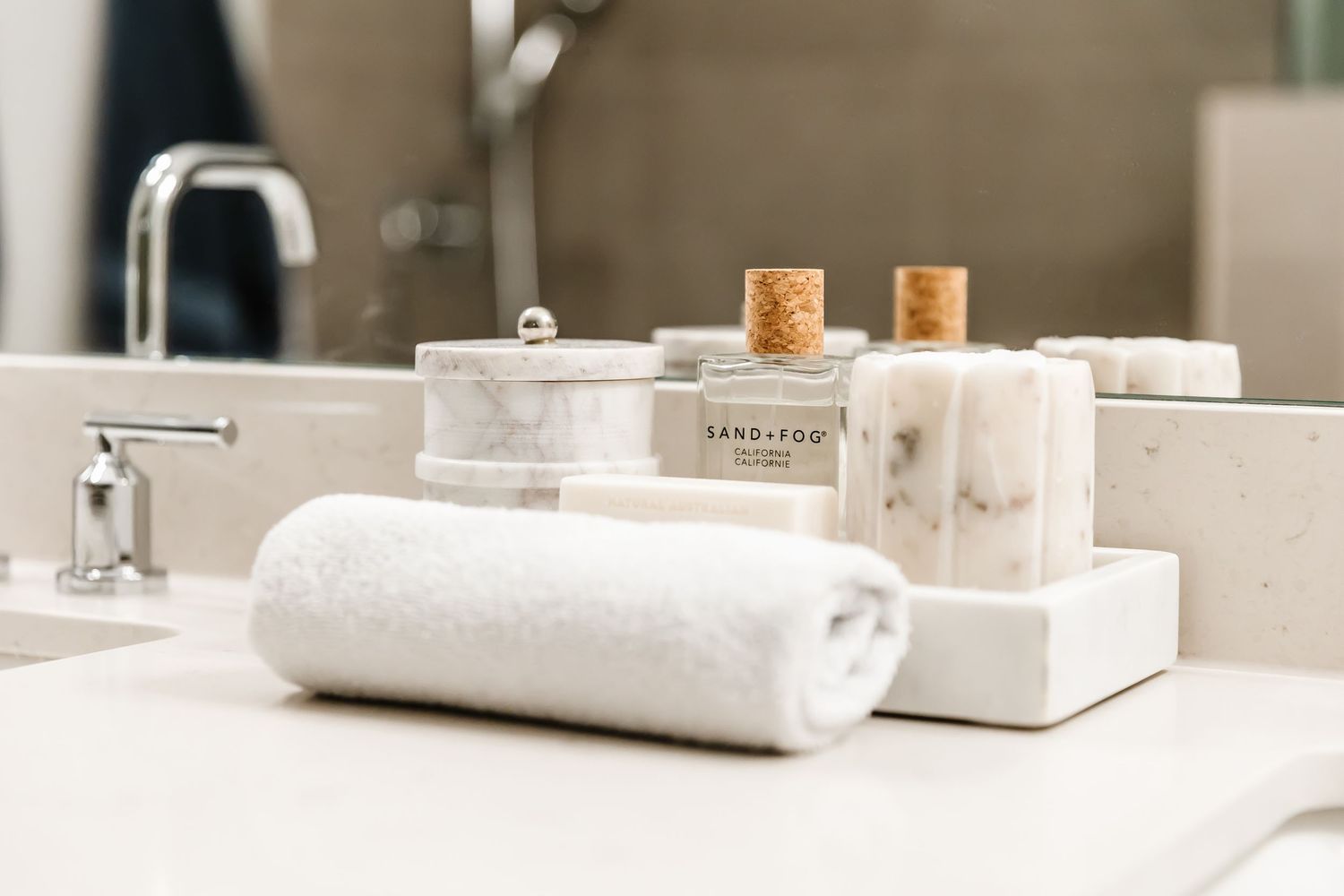 Minimalist white bathroom counter with towels, soap dispenser, and decorative glass jars arranged neatly on marble surface.