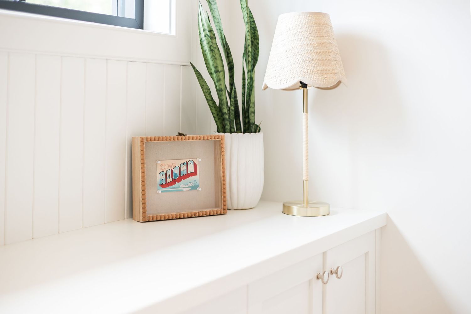 Minimalist white shelf styling with lamp, plant and framed artwork against bright wall in a west Kelowna Airbnb