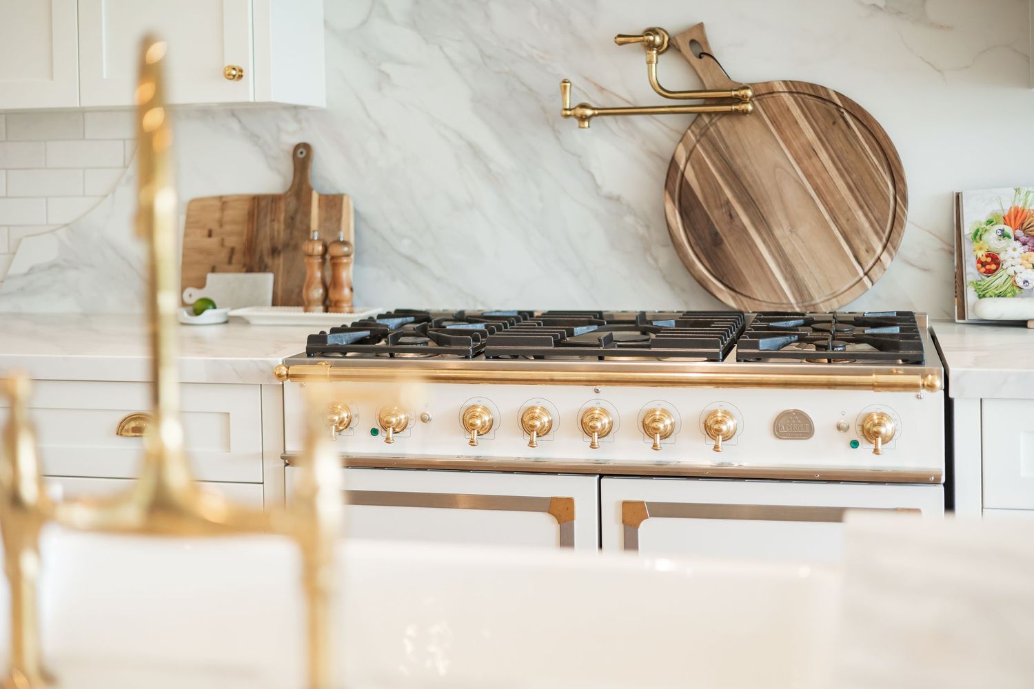Modern kitchen with white cabinets, marble countertops, and gold hardware accents showcases a sleek gas cooktop in a west Kelowna Airbnb
