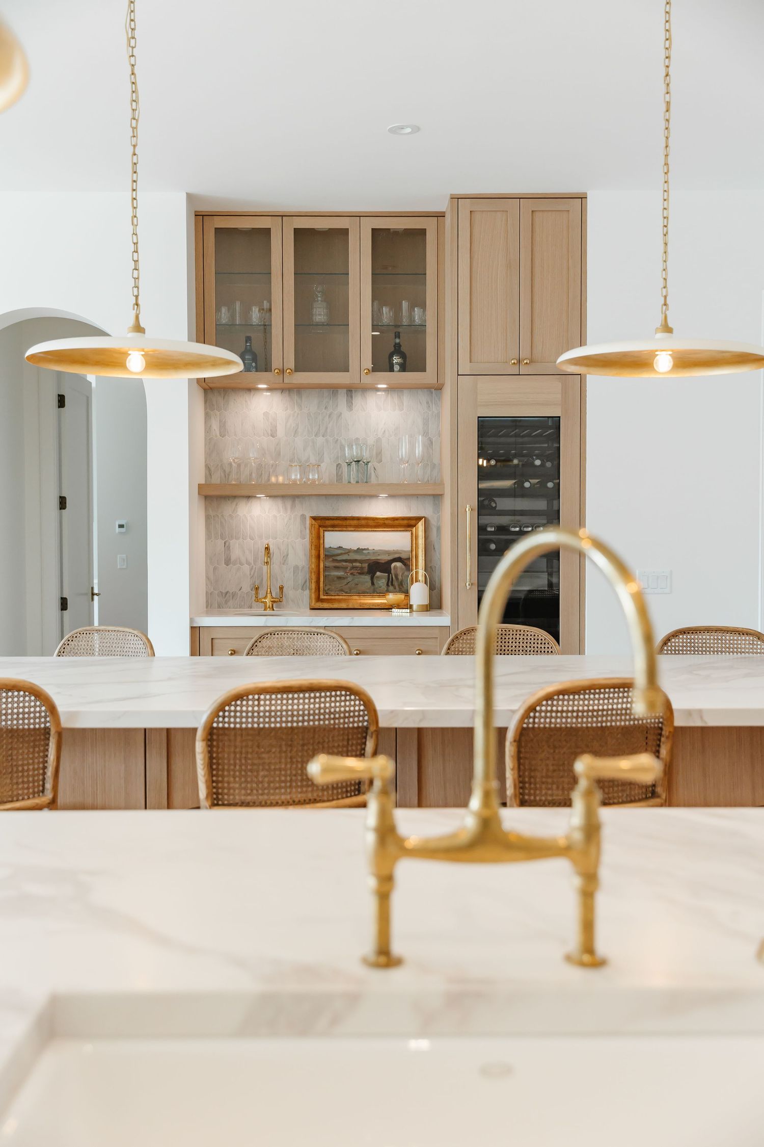 Modern kitchen with light wood cabinets, gold pendant lights, and white marble countertops creates an elegant cooking space in a Kelowna