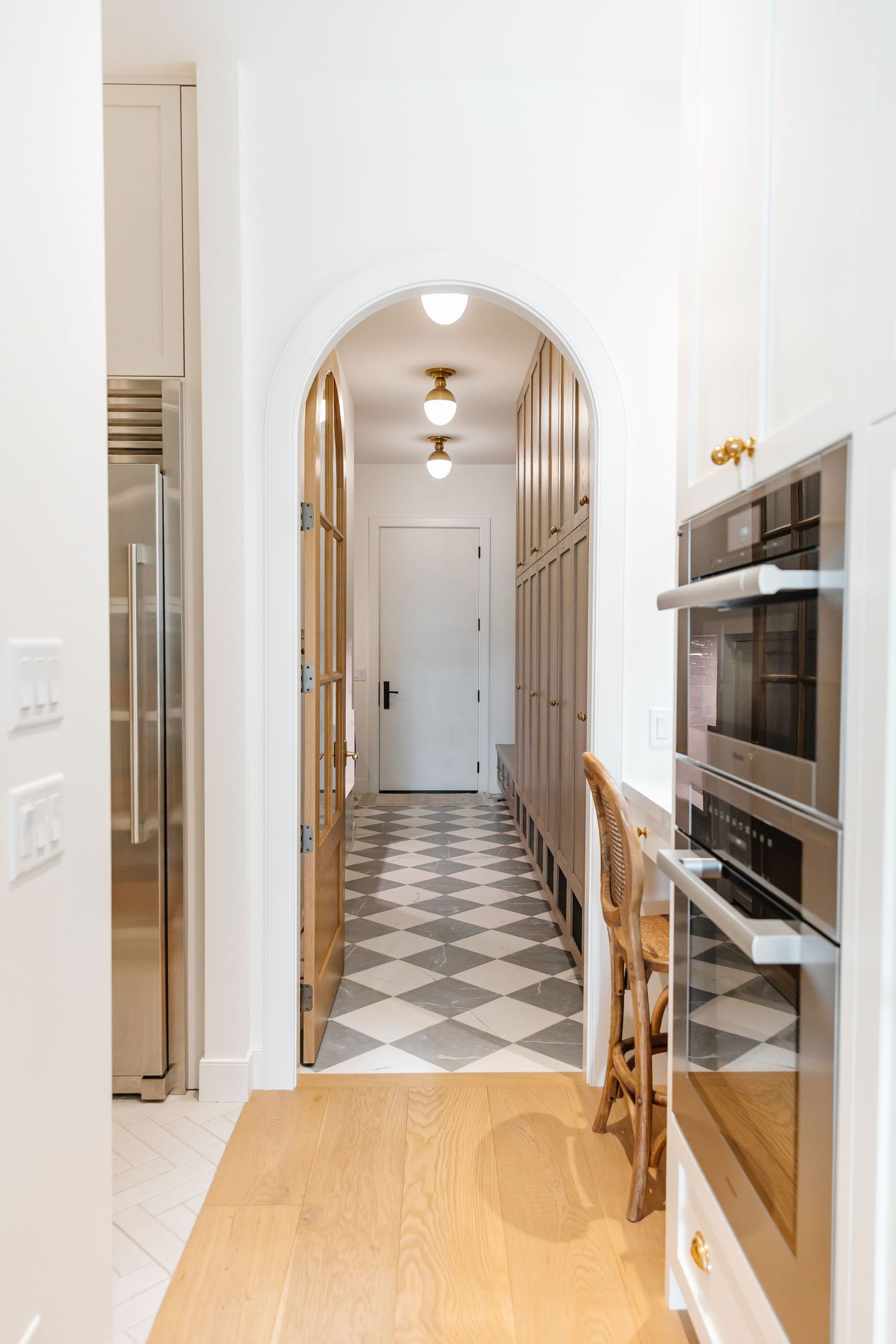 Hallway featuring checkered floor tiles, white walls, and wooden accents leads to multiple doorways in a west Kelowna Airbnb