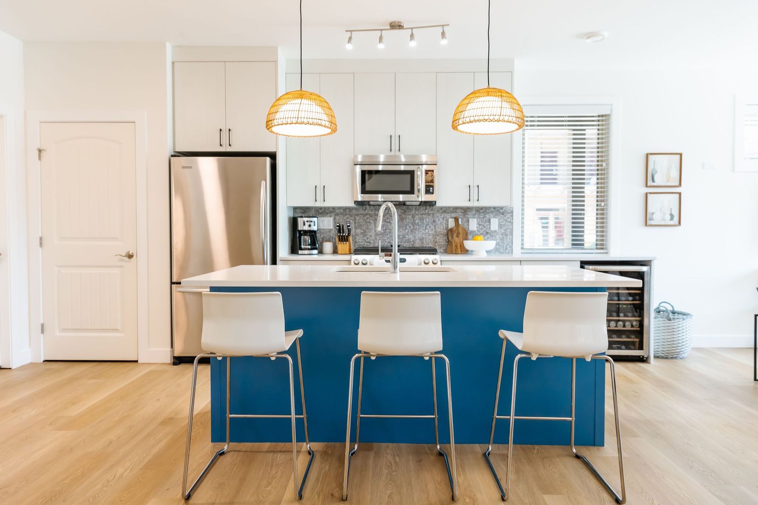 Contemporary kitchen with blue island and white bar stools in open concept space.