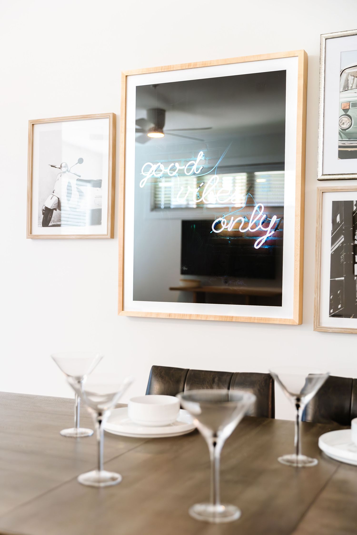 Modern dining area with wine glasses and framed artwork on white walls.