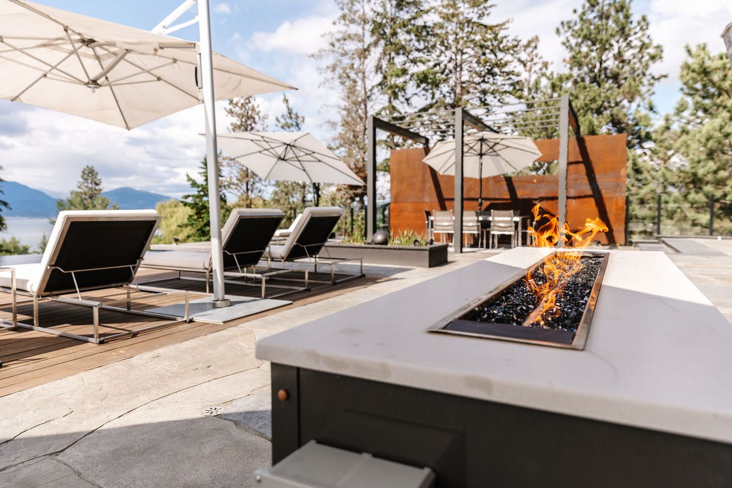 Modern outdoor patio deck with lounge chairs and linear fire pit overlooking mountain views.