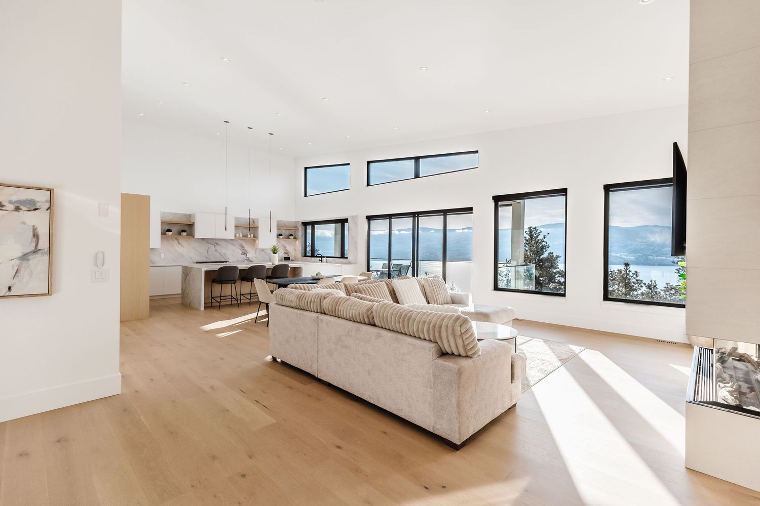 Modern coastal living room with light hardwood floors, beige sectional sofa and large windows offering ocean views.