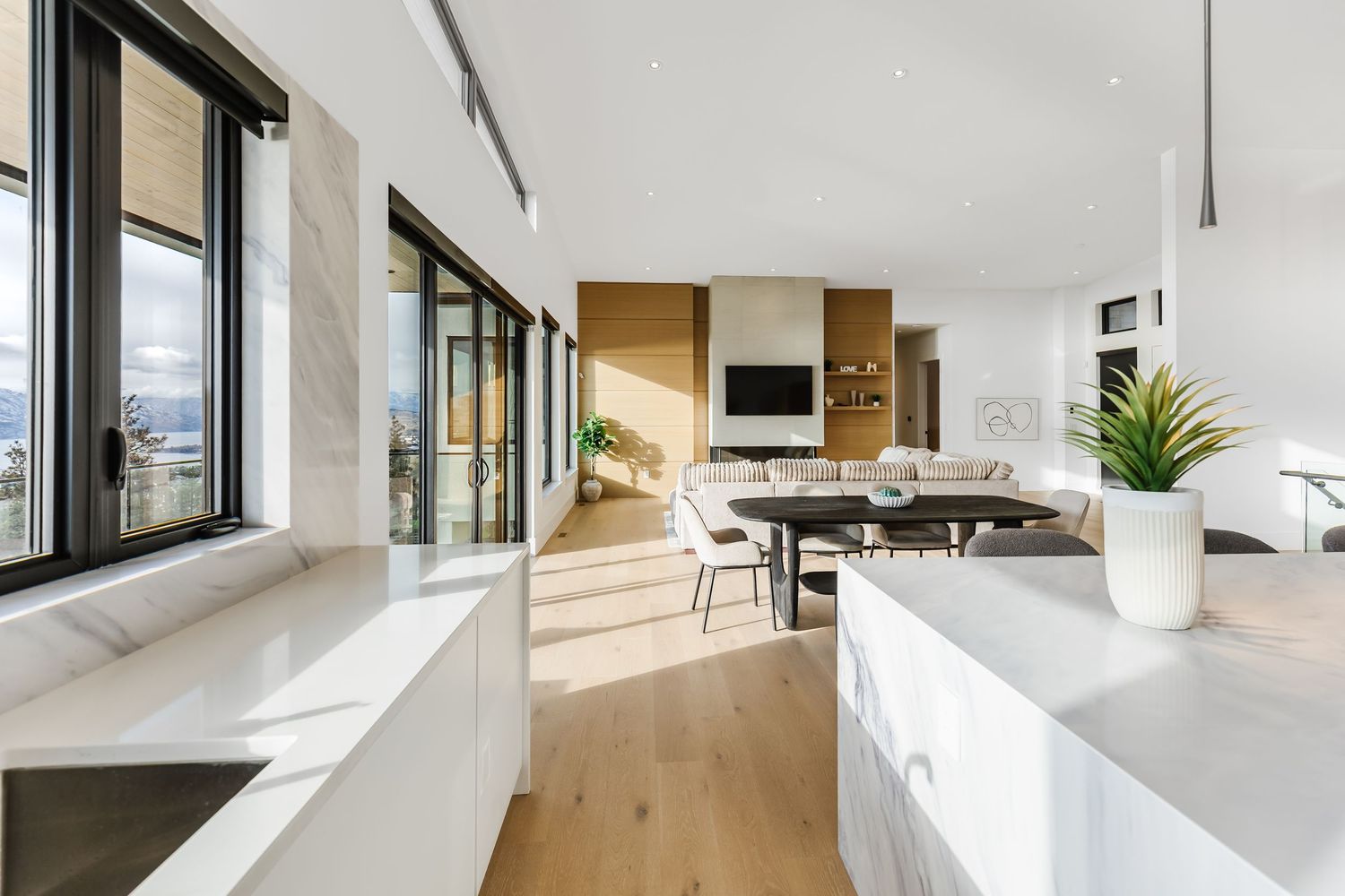 Modern open concept kitchen with white countertops, light wood floors and large windows offering natural light.