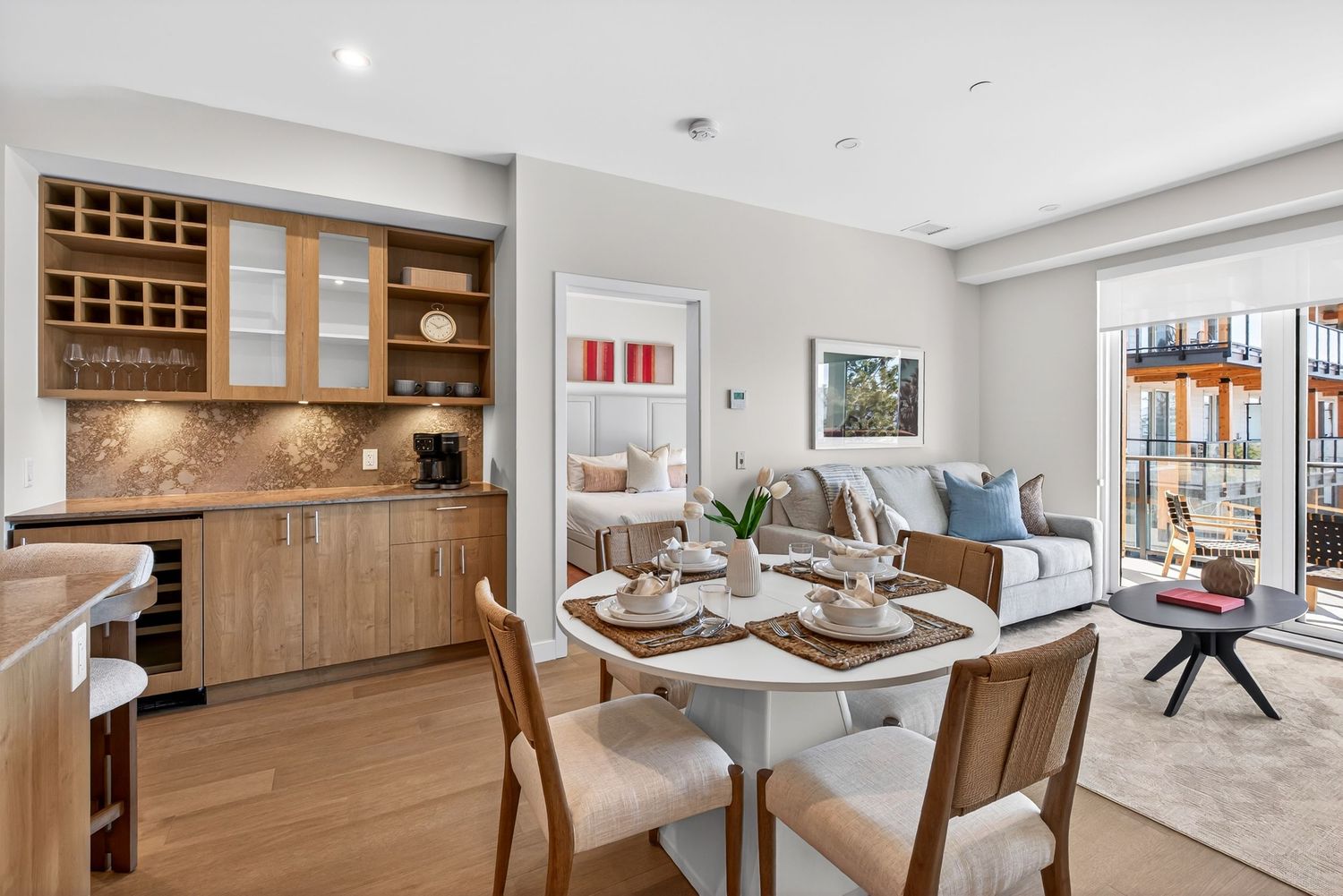 Modern open-plan dining and living room with wood cabinetry, built-in wine rack, and sliding glass doors to a balcony.