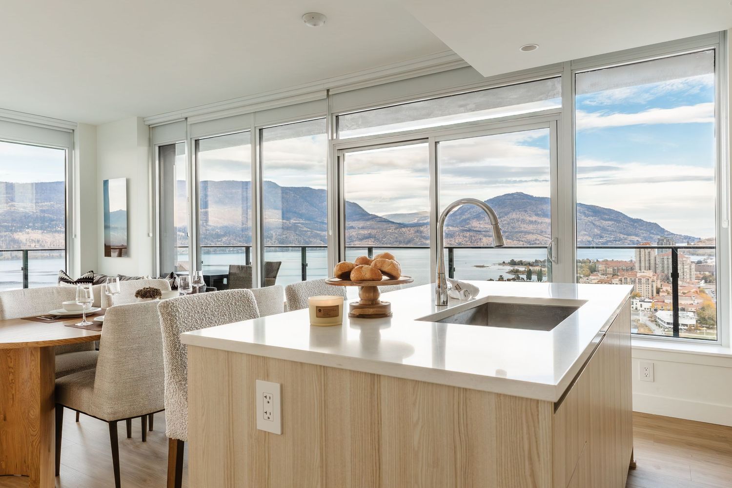 Modern open concept apartment interior with floor-to-ceiling windows showcasing mountain views and contemporary furnishings.