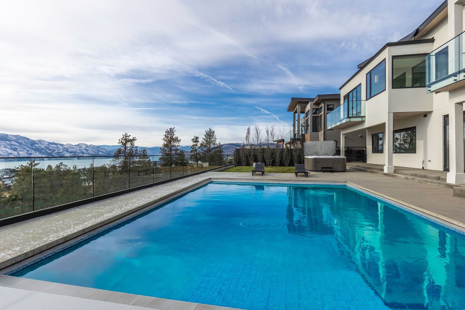 A panoramic view of an infinity pool overlooking snow-capped mountains with blue skies and white clouds in the background.