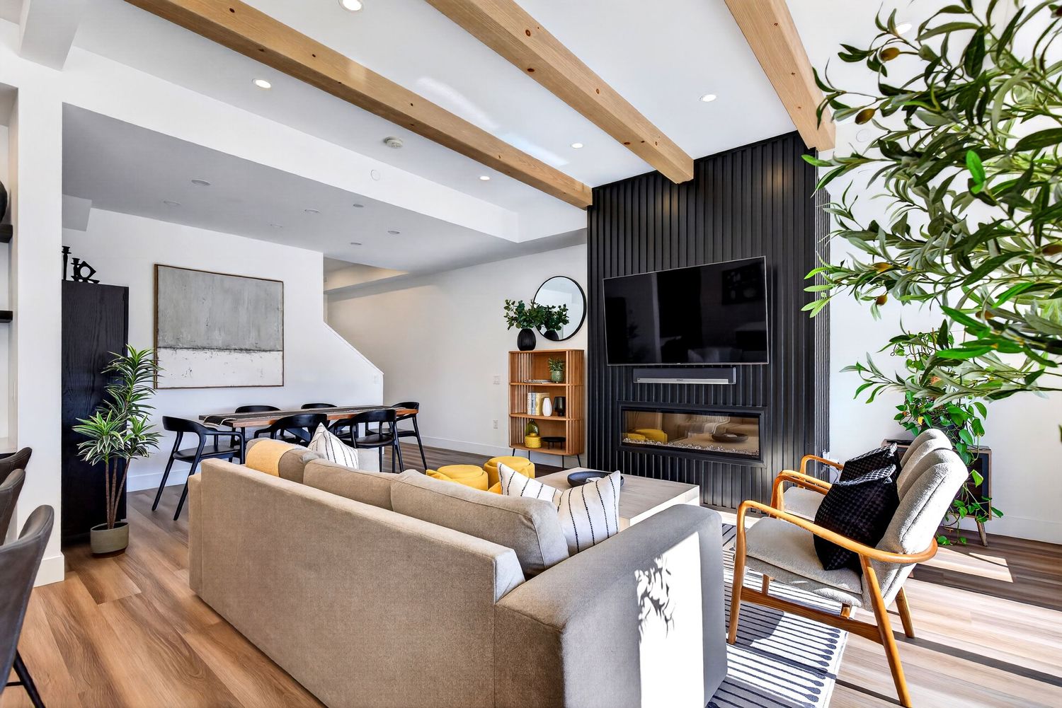 Modern living room with wood beam ceiling, black slat fireplace wall, mounted TV, gray sofa, and hardwood floors.
