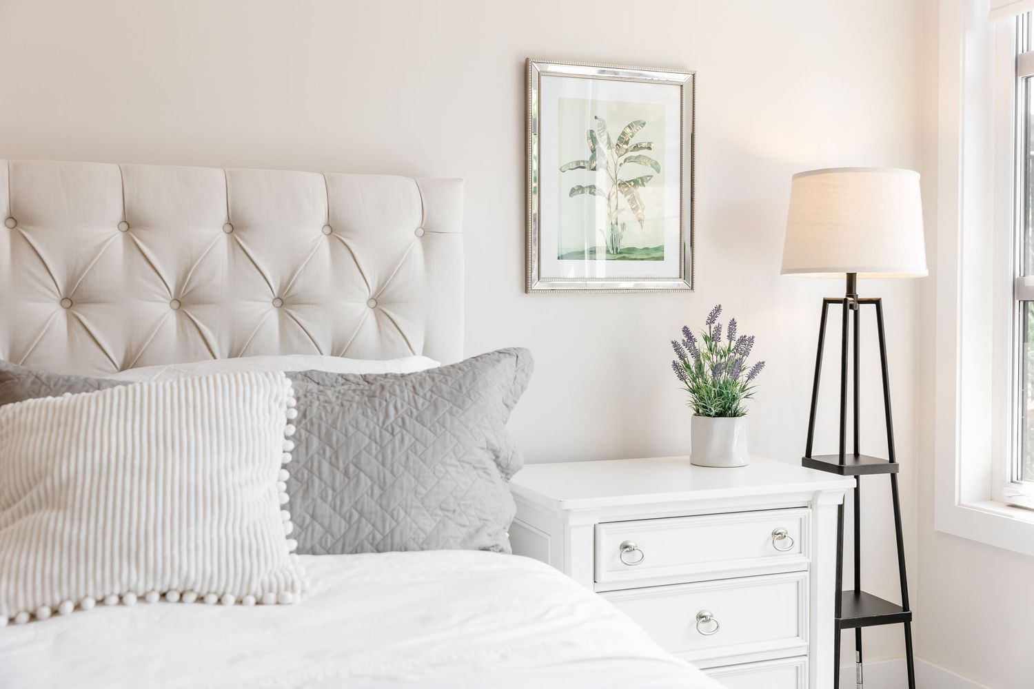 Bright white bedroom with plush bedding, decorative pillows, and natural light streaming through windows.