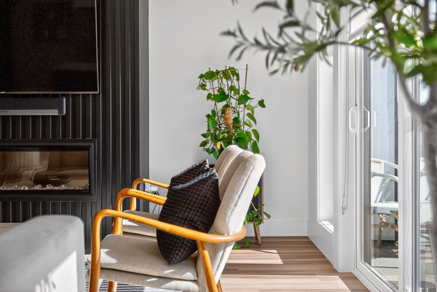 Modern living room corner with yellow armchair, trailing pothos plant, black fireplace, and glass door to balcony.