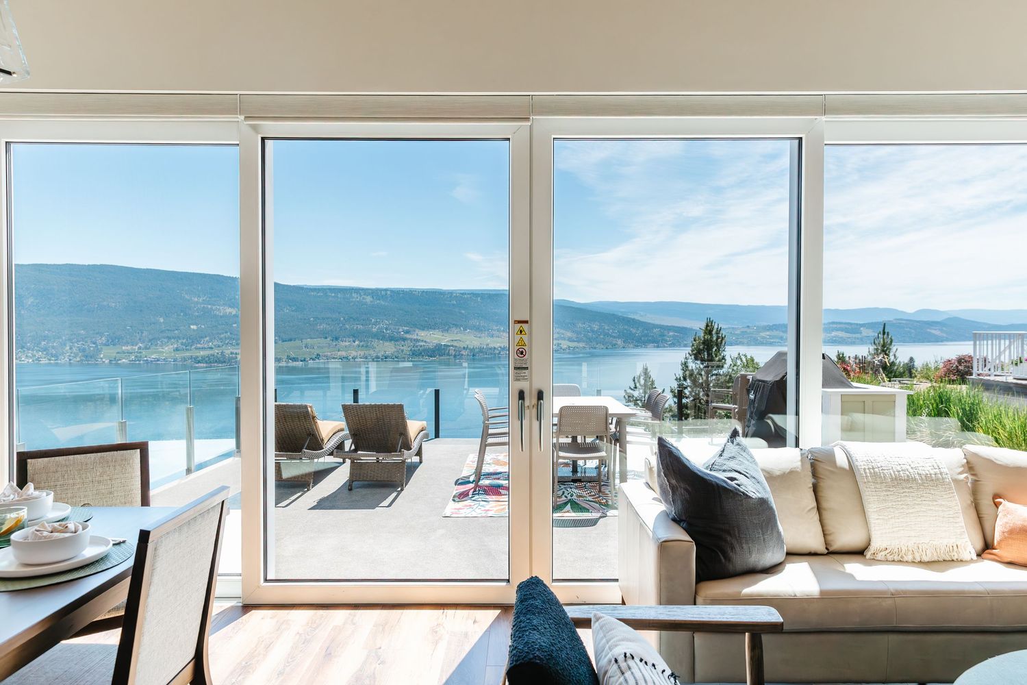 Luxurious living room with floor-to-ceiling windows overlooking a scenic lake and mountain view from a modern balcony in Kelowna BC