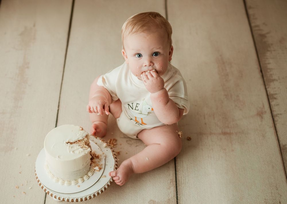 Simple cake smash photo setup with white frosted cake on wooden floor.