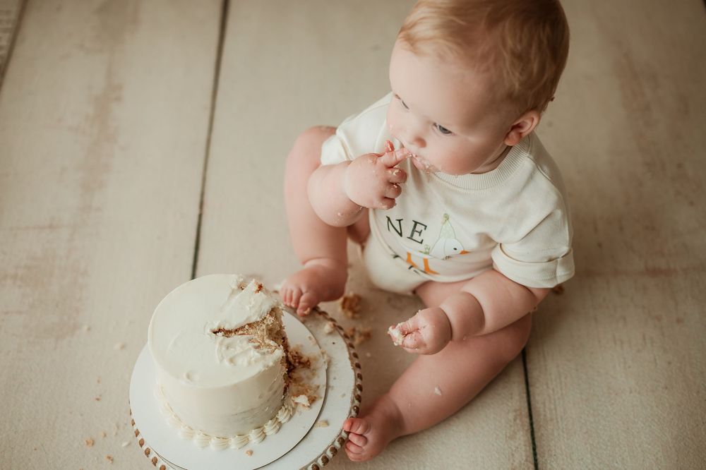 Baby exploring and playing with white birthday cake during cake smash photo session.