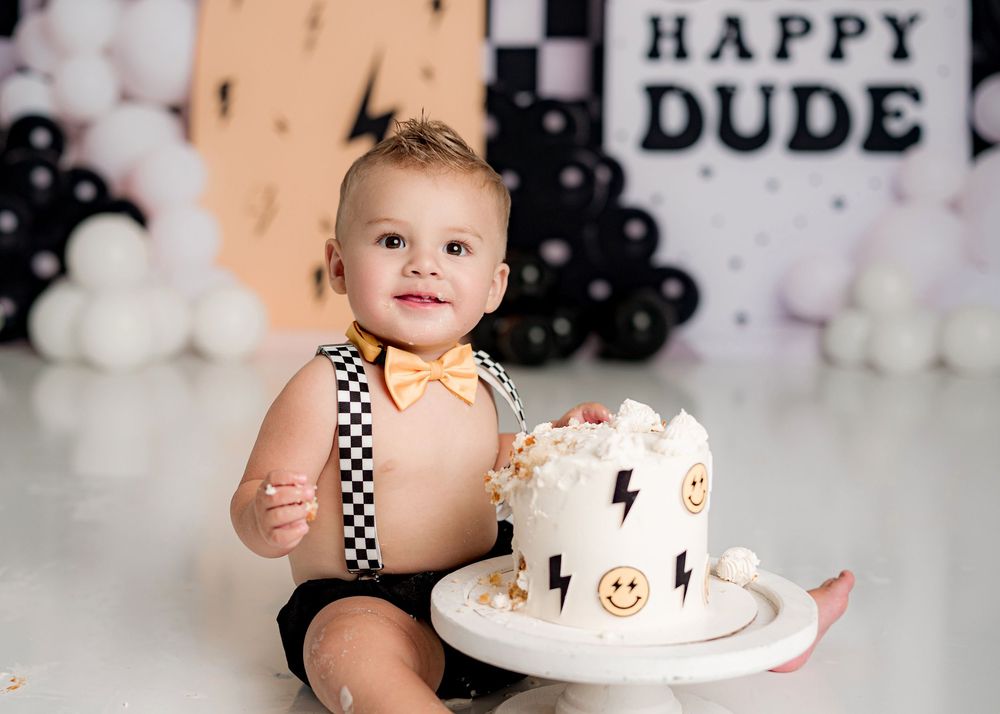 A first birthday party setup with black and white checkered decorations and a smash cake against a balloon backdrop.