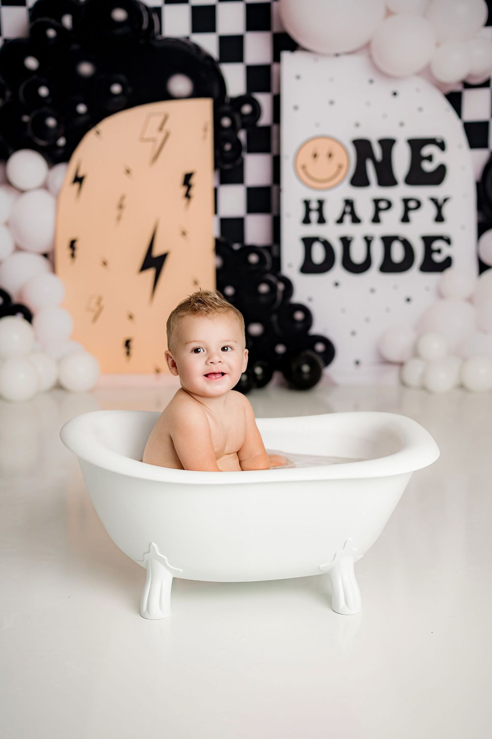 Baby photo shoot with black and white decor featuring a small white bathtub and lightning bolt backdrop.
